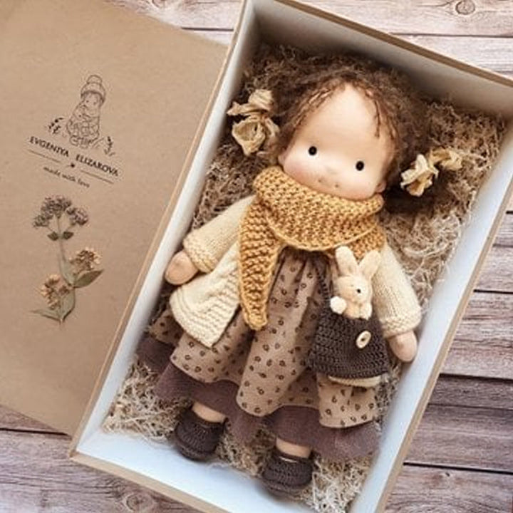 "Handgefertigte Waldorfpuppe in Erdtönen, mit rotem Haar, braunem Kleid und blauem Hut, sicher und natürlich."