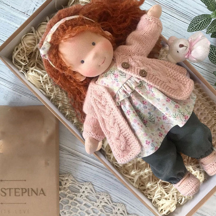 "Handgefertigte Waldorfpuppe in Erdtönen, mit rotem Haar, braunem Kleid und blauem Hut, sicher und natürlich."